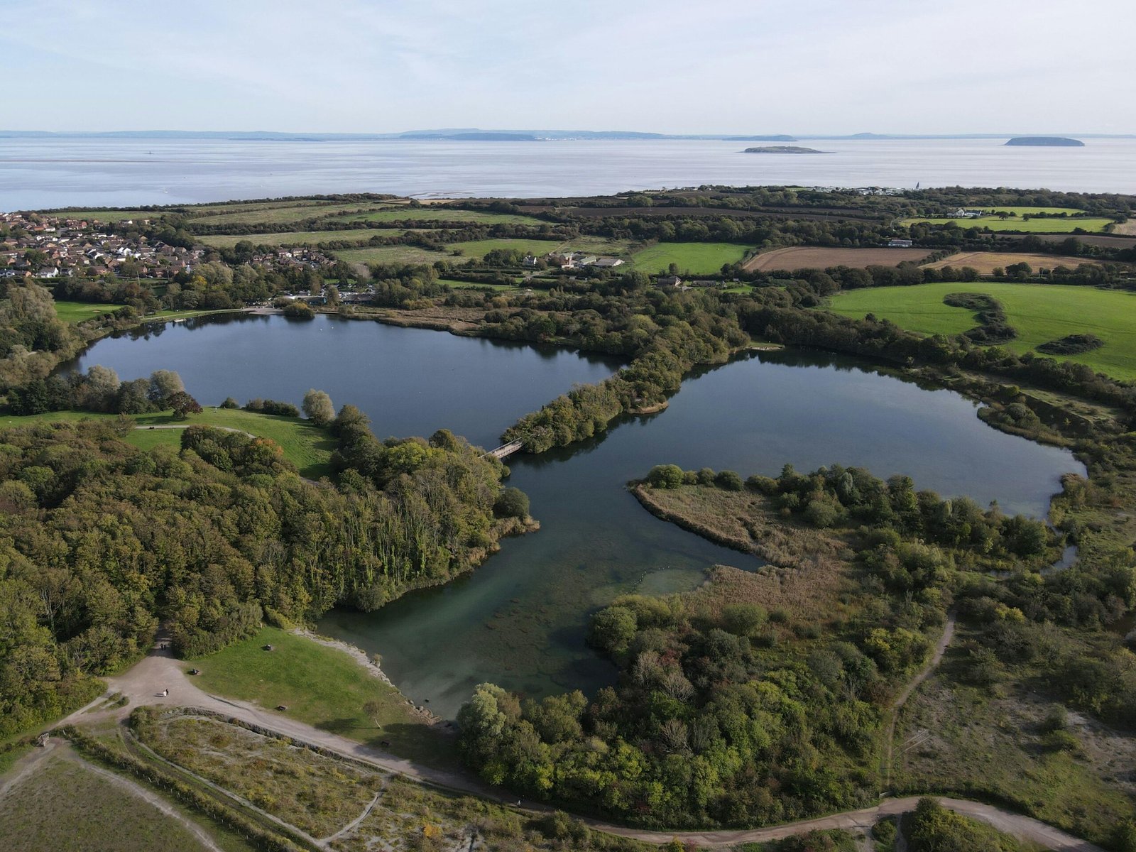 Aerial shot of Cosmeston Lakes with green landscapes, dense trees, and serene water bodies in Wales.